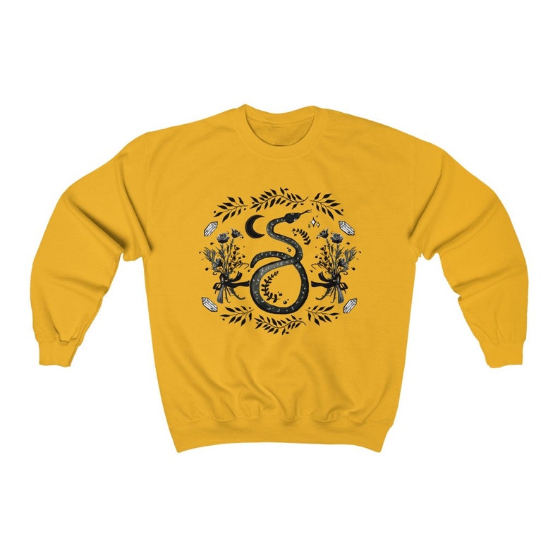 May include: A yellow sweatshirt with a black and white illustration of a snake with a crescent moon and flowers. The snake is curled up and has a floral design around it.