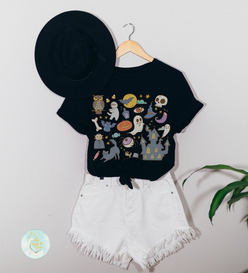 Pode incluir: Camiseta preta com uma estampa gr&aacute;fica colorida com tema de Halloween que apresenta uma variedade de personagens e objetos assustadores, incluindo um fantasma, um morcego, uma ab&oacute;bora, um chap&eacute;u de bruxa e uma casa assombrada. A camiseta &eacute; combinada com shorts jeans brancos.