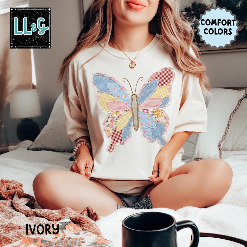 Peut inclure: T-shirt de couleur ivoire avec un grand motif de papillon sur le devant. Le papillon a des ailes en patchwork dans les tons de bleu, rose, jaune et rouge. Le t-shirt porte les inscriptions "COMFORT COLORS" et "LL&G" dans le coin sup&eacute;rieur gauche.