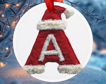 Könnte beinhalten: Ein weißer Keramik-Anhänger mit einer roten Weihnachtsmütze und einem weißen Pelzbesatz. Der Buchstabe "A" befindet sich in der Mitte des Anhängers, mit einem weißen Pelzbesatz um den Buchstaben.