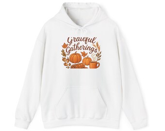 May include: White hooded sweatshirt with a front pocket. The graphic on the front features the text "Grateful Gatherings" surrounded by pumpkins, leaves, acorns, and a cup of coffee. The design is in shades of orange, brown, and beige.