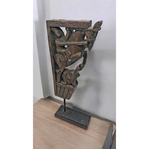 May include: A carved wooden corbel featuring a figure riding a horse, with an elephant at the base. The corbel is mounted on a black metal stand.