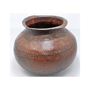 May include: A large, round, brown leather pot with metal accents. The pot has a wide opening and is decorated with metal studs around the rim and body.