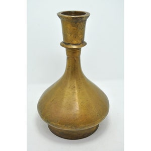 May include: A brass candlestick with a wide, flared base and a narrow, cylindrical top. The candlestick has a smooth, polished finish.