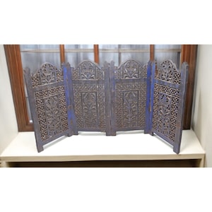 May include: A four-panel wooden screen with intricate floral carvings. The screen is painted in a distressed blue and brown color scheme. The panels are connected by hinges, allowing them to fold. The screen is a decorative room divider.
