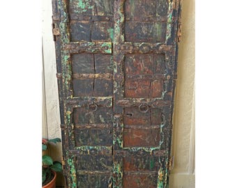 May include: A pair of antique wooden doors with a distressed finish. The doors are primarily dark brown with accents of green and rust-colored paint. Metal hardware and ring pulls are visible.