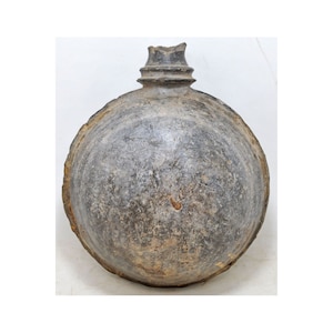 Puede incluir: Una botella de cerámica gris con cuerpo redondeado y cuello estrecho. La botella tiene una superficie rugosa y texturizada y parece bastante antigua.