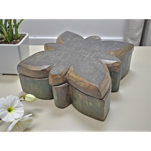 May include: A large, wooden box in the shape of a flower. The box is painted in shades of gray and green, with visible wood grain. The box is likely used for storage or decoration.