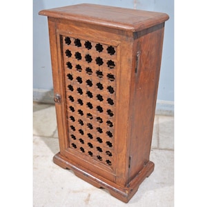 May include: A small, wooden cabinet with a single door. The door features a decorative, carved pattern of stars. The cabinet is a rich brown colour and has a simple, elegant design.