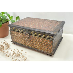 May include: A rectangular wooden box with a hinged lid. The box features a detailed pattern in shades of brown and gold. The lid and sides are adorned with intricate designs, and the box has a metal clasp. The box is likely used for storage.