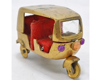 May include: A small, gold-colored metal model of an auto rickshaw with red velvet seats and a clear plastic windshield. The model has purple and orange accents.