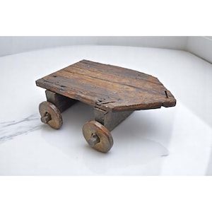 May include: A rustic, wooden toy cart with a weathered appearance. The cart features a rectangular platform made of aged planks and two sets of wooden wheels. The wood has a rich, brown color with visible grain and imperfections.