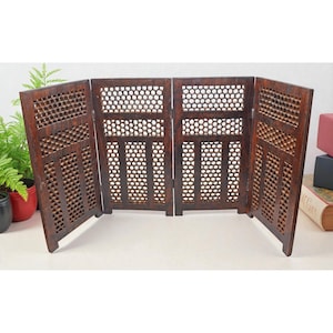 May include: A four-panel, dark brown wooden room divider. Each panel features a decorative, openwork design with geometric patterns. The divider is freestanding and suitable for creating privacy or adding a decorative element to a room.