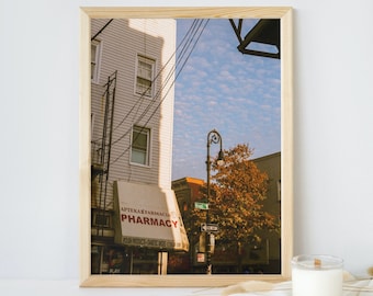 Peut inclure: Une photographie encadrée d'une scène de rue de la ville avec une devanture de pharmacie. L'enseigne de la pharmacie indique "Apteka Farmacia Pharmacy" en lettres rouges. Le bâtiment est blanc avec un auvent brun. Il y a un lampadaire et un arbre en arrière-plan.