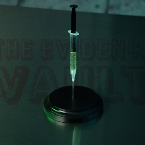 Puede incluir: Una jeringa negra con un l&iacute;quido verde en su interior est&aacute; de pie sobre una base circular negra. El fondo es de color verde oscuro con el texto "THE EVIDENCE VAULT" en negro.