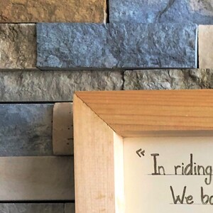 May include: A wooden frame with a white background and handwritten text that reads "In riding we bond".