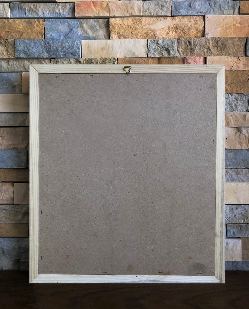 May include: A wooden picture frame with a brown cardboard backing. The frame is hanging on a wall made of stacked stone tiles.