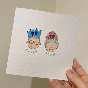Puede incluir: Tarjeta de felicitaci&oacute;n dibujada a mano con dos caras de dibujos animados, cada una con una corona con el n&uacute;mero 79. Los nombres "Allen" y "Joan" est&aacute;n escritos debajo. La tarjeta es blanca con una superficie texturizada.