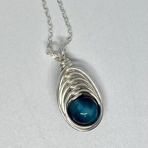 May include: A silver chain necklace with a blue gemstone pendant. The pendant is wrapped in silver wire and has a teardrop shape.