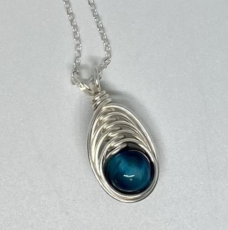 May include: A silver chain necklace with a blue gemstone pendant. The pendant is wrapped in silver wire and has a teardrop shape.