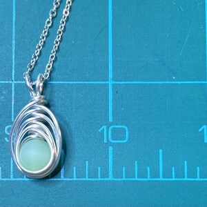 May include: A silver chain necklace with a pendant featuring a light green stone wrapped in silver wire.