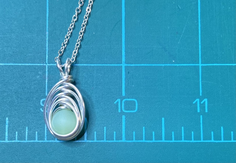 May include: A silver chain necklace with a pendant featuring a light green stone wrapped in silver wire.