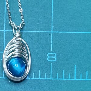 May include: A silver chain necklace with a pendant featuring a blue gemstone wrapped in silver wire.
