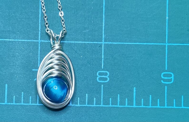 May include: A silver chain necklace with a pendant featuring a blue gemstone wrapped in silver wire.