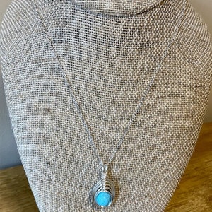 Op de afbeelding: Een turquoise stenen ketting en oorbellen set met zilveren draadwikkeling. De ketting heeft een hanger met een turquoise steen gewikkeld in zilveren draad. De oorbellen zijn ook gemaakt met turquoise stenen gewikkeld in zilveren draad.