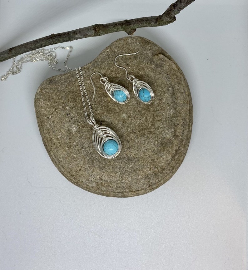Op de afbeelding: Een turquoise edelsteen ketting met bijpassende oorbellen. De hanger en oorbellen zijn gemaakt van zilverdraad gewikkeld rond de turquoise stenen.