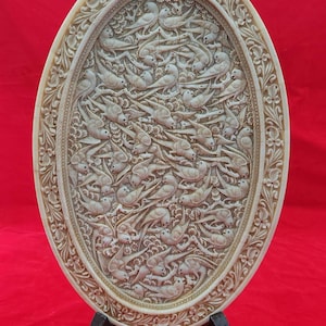 May include: An oval-shaped, cream-colored, decorative plate with intricate carvings of birds and floral designs. The plate is on a black stand.