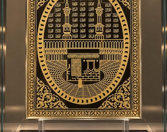 May include: A rectangular wall art piece featuring a gold-on-black illustration of the Kaaba in Mecca. The design includes intricate Arabic calligraphy, geometric patterns, and a decorative border, all encased in a thin gold frame.
