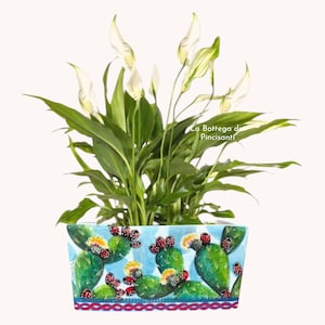 May include: A potted peace lily with white flowers and green leaves. The rectangular ceramic pot is painted with a cactus design in shades of blue, green, red, and yellow. The text "La Bottega di Pincisanti" is visible on the pot.