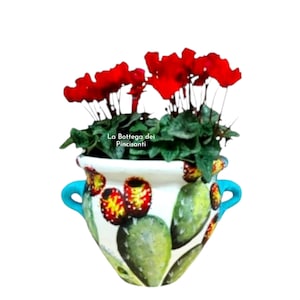 Op de afbeelding: Witte keramische plantenbak met een cactusontwerp en turkooizen handvatten, met rode bloemen en groen blad. De plantenbak heeft een handgeschilderd ontwerp van groene cactussen en rood en geel fruit. De tekst "La Bottega dei Pincisanti" is zichtbaar.
