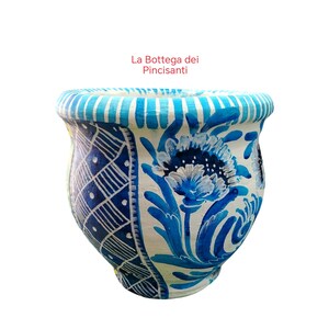 May include: A hand-painted ceramic pot with a white base and blue floral and geometric designs. The rim features blue and white stripes. The text "La Bottega dei Pincisanti" is visible.
