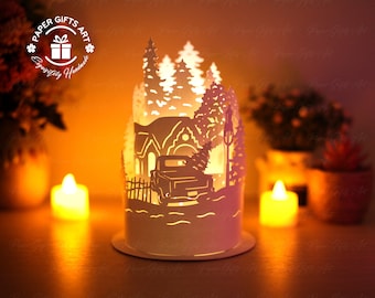 Może przedstawiać: Biała lampion z papieru przedstawiająca zimową scenę. Scena zawiera dom, ciężarówkę i drzewa. Lampion jest oświetlony od wewnątrz, tworząc ciepłe światło.