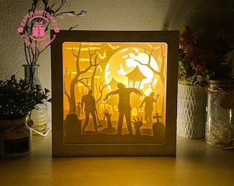 May include: A wooden shadow box with a Halloween scene featuring three zombies walking through a graveyard under a full moon. The scene is illuminated from behind, creating a glowing effect.