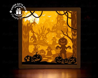 Może przedstawiać: Świetlna skrzynka z papieru o tematyce Halloween. Projekt przedstawia nawiedzony dom, dynie, duchy i pełnię księżyca. Grafika jest podświetlana od wewnątrz, tworząc ciepłą poświatę. Widoczny jest tekst "Paper Gifts Art".
