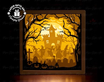 May include: A Halloween-themed paper art shadow box with a spooky castle, witches, pumpkins, and a graveyard. The artwork is illuminated from within, creating a warm, inviting glow. The box is square and has the text "Paper Gifts Art" and "Exquisitely Handmade".