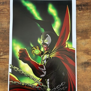 May include: A comic book character, Spawn, with a red cape and a black and white suit, is holding a glowing green orb. He is surrounded by green flames and chains.