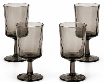 May include: A set of four smoke-colored glass goblets featuring a distinct wavy, rippled texture on the bowl. Each glass has a smooth, cylindrical stem and a circular base, crafted from translucent dark gray glass with a consistent finish.
