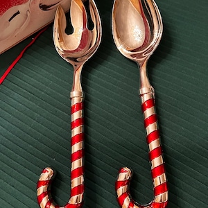 Könnte beinhalten: Ein versilbertes Salatbesteck bestehend aus einer Gabel und einem Löffel mit Griffen im rot-weiß gestreiften Zuckerstangen-Design. Das Set befindet sich in einer Schachtel mit der Aufschrift Silver Plated Candy Cane Design Salad Spoon and Fork Set.
