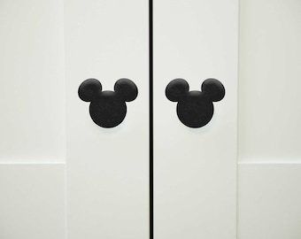Op de afbeelding: Twee zwarte Mickey Mouse-kopvormige kastdeurknopjes op een witte deur.