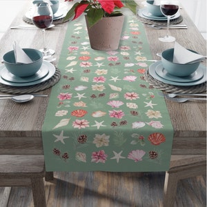 Może przedstawiać: Zielony bieżnik stołowy z powtarzającym się wzorem muszli, rozgwiazd, szyszek i gwiazd betlejemskich. Bieżnik leży na drewnianym stole z dwoma nakryciami.