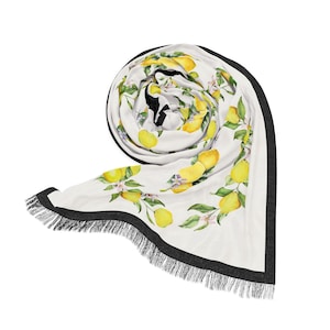 May include: White round beach towel with a lemon and floral pattern. The towel has a black border with fringe. The design features yellow lemons, green leaves, and white flowers. The towel is rolled up, showing the pattern.