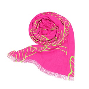 May include: A rolled-up, hot pink scarf with a neon green leaf design. The scarf has a fringed edge and is displayed against a white background. The scarf is made of a soft material.