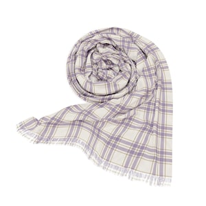 May include: A rolled-up scarf with a plaid pattern in lavender, cream, and gold. The scarf has a fringed edge and is made of a soft, lightweight material. The scarf is a fashion accessory.