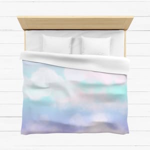 Può includere: Un letto bianco con un copripiumino tie-dye blu chiaro, rosa e verde. Il letto ha una testiera in legno e due cuscini bianchi.