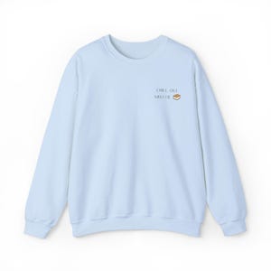 Op de afbeelding: Een lichtblauw sweatshirt met lange mouwen. De tekst "CHILL OUT SWEETIE" staat rechtsboven, vergezeld van een kleine koekjesafbeelding. Het sweatshirt is gemaakt van een zacht materiaal.