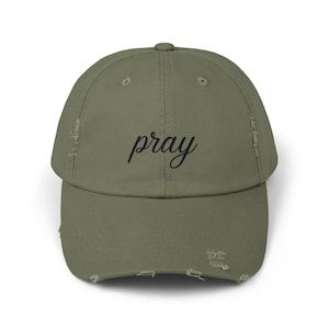 May include: A green distressed baseball cap with the word "pray" embroidered in black on the front.